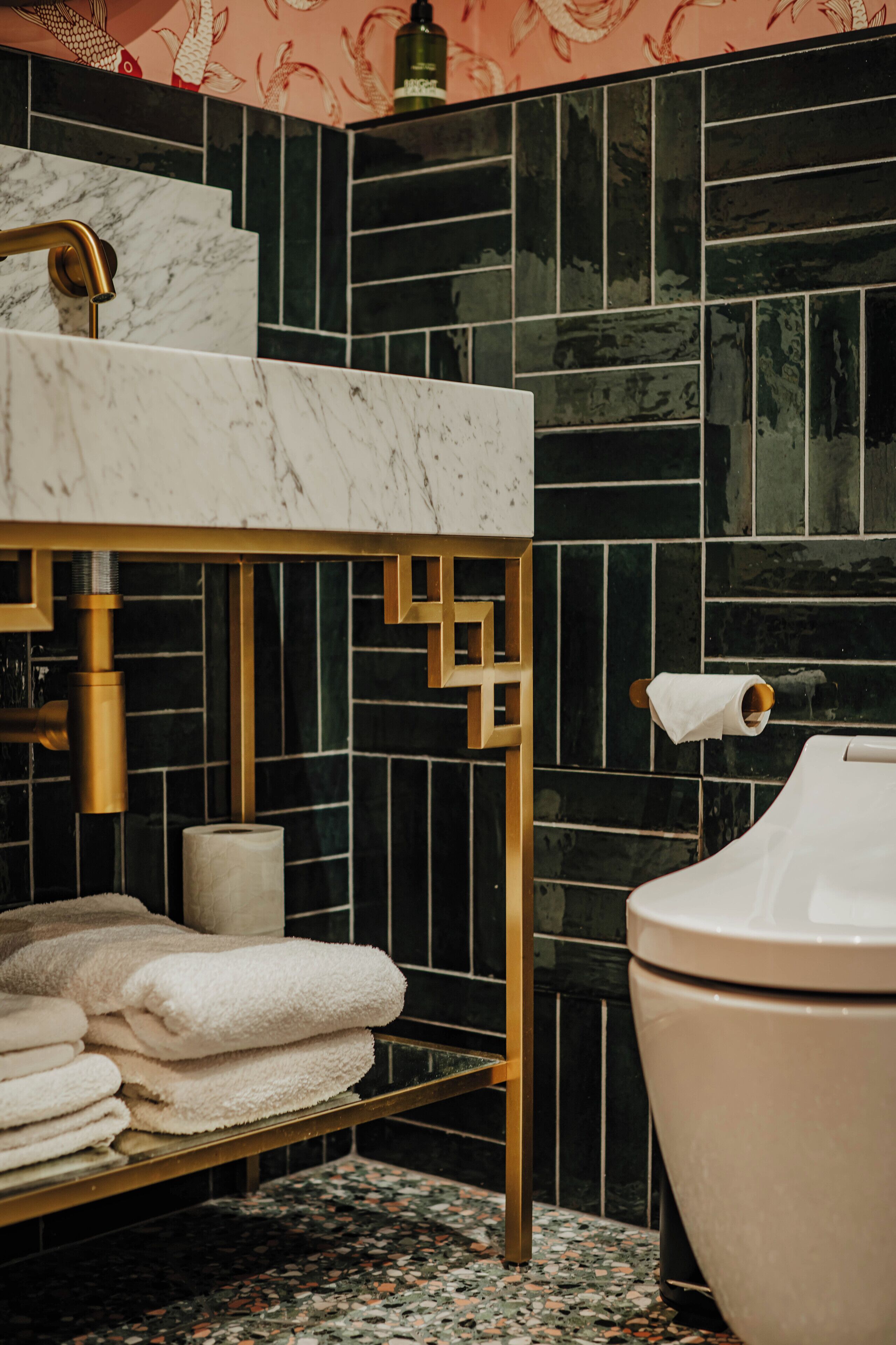 A bathroom with a marble sink, black tiled walls, a toilet, and a towel rack.