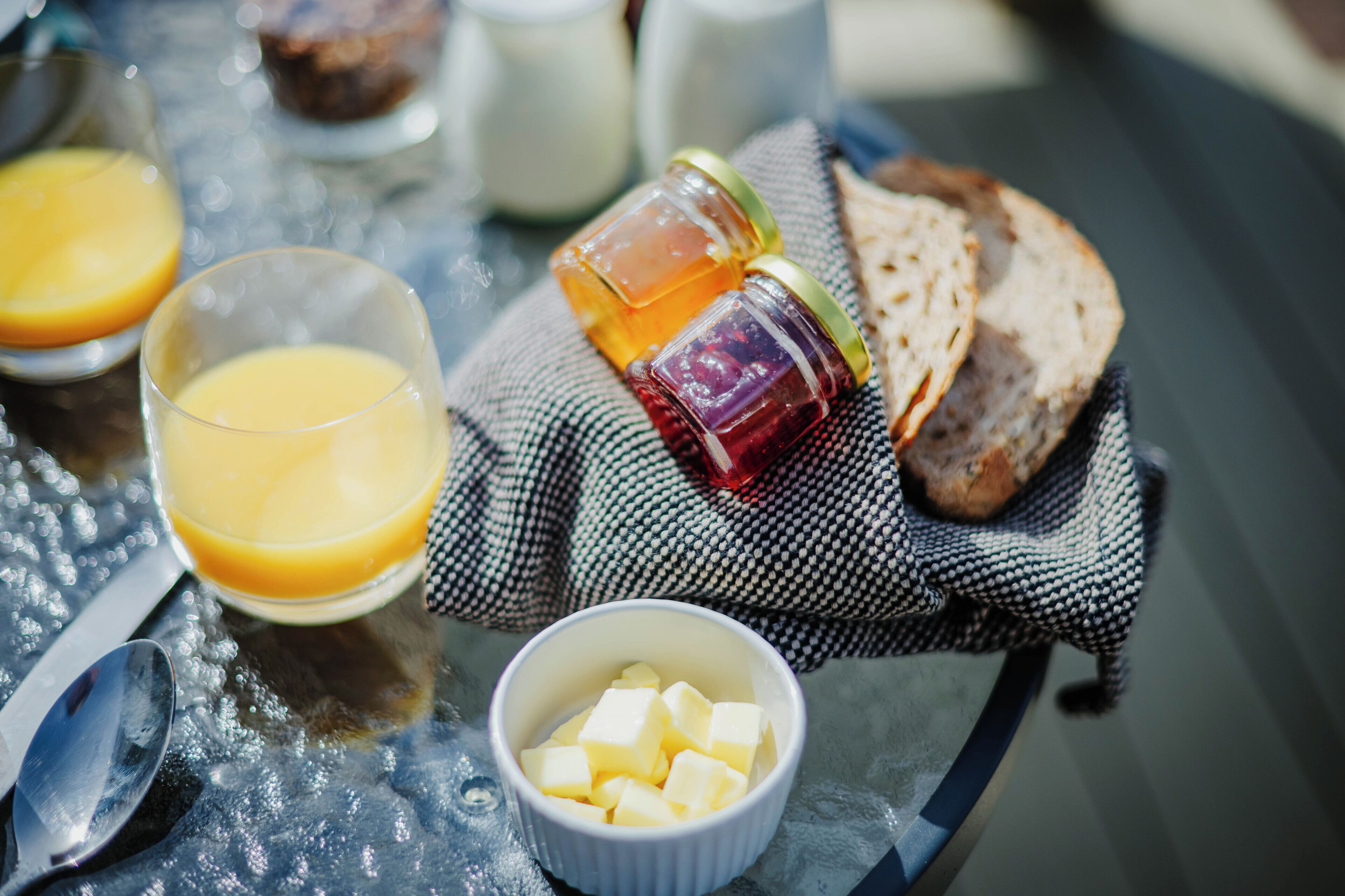Une table dressée pour le petit-déjeuner, avec des toasts, du beurre, du miel et du jus d’orange.