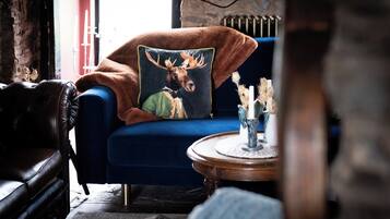 A cozy room with a blue armchair, a decorative pillow with a moose, and a small round wooden table with candles.