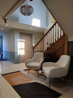 A spacious living area with a high ceiling, a wooden staircase, and two armchairs.