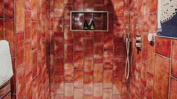 Ducha a ras de suelo con azulejos rojos, un banco de ducha blanco y un estante pequeño con botellas.
