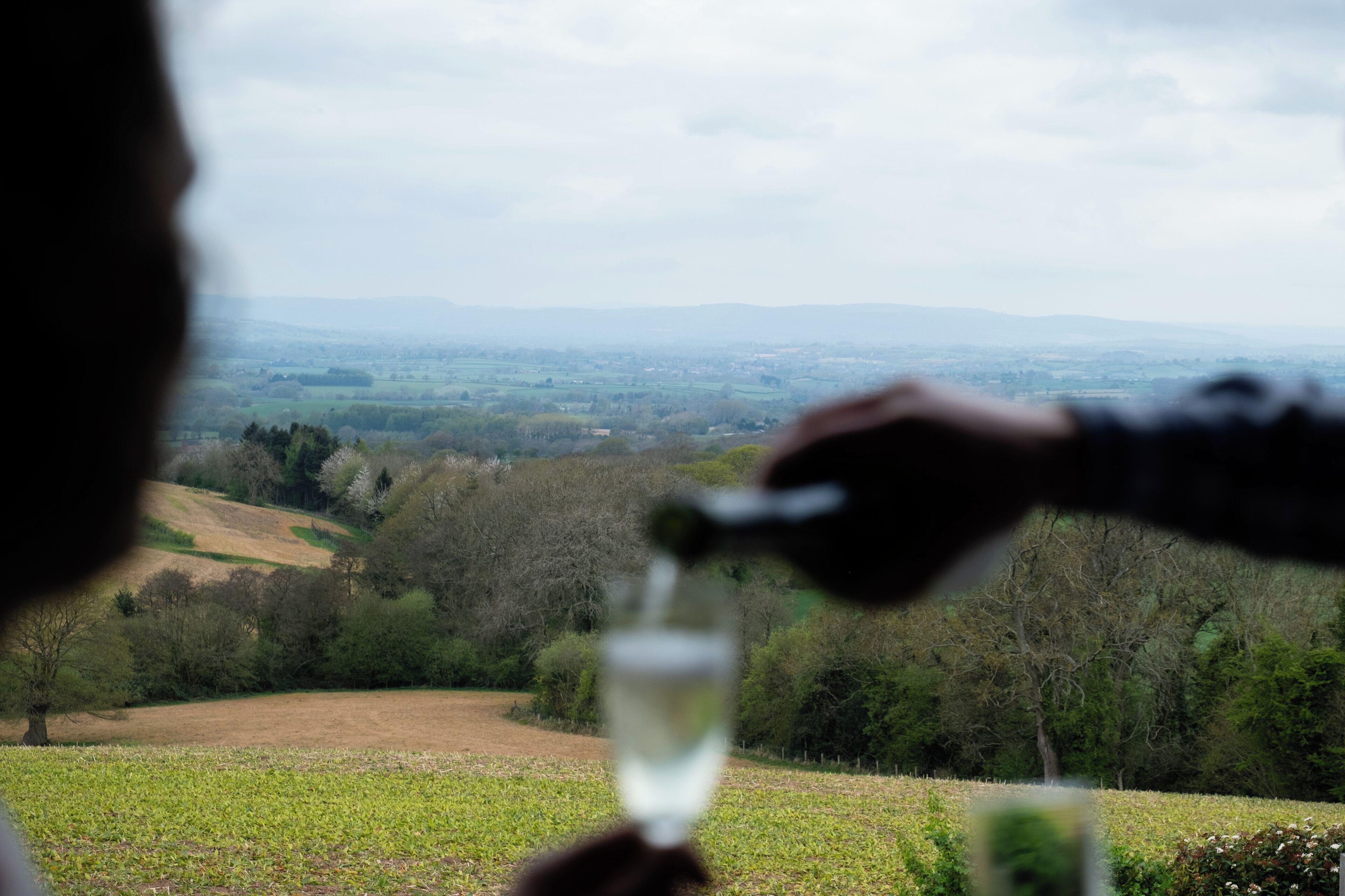 Une personne tenant un verre d’eau, avec en arrière-plan un paysage pittoresque d’une vallée et de collines.