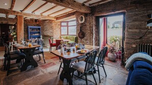 A rustic dining area with a wooden table and chairs, a stone wall, and a view of the outside. - Hanley House (Tenbury Wells)
