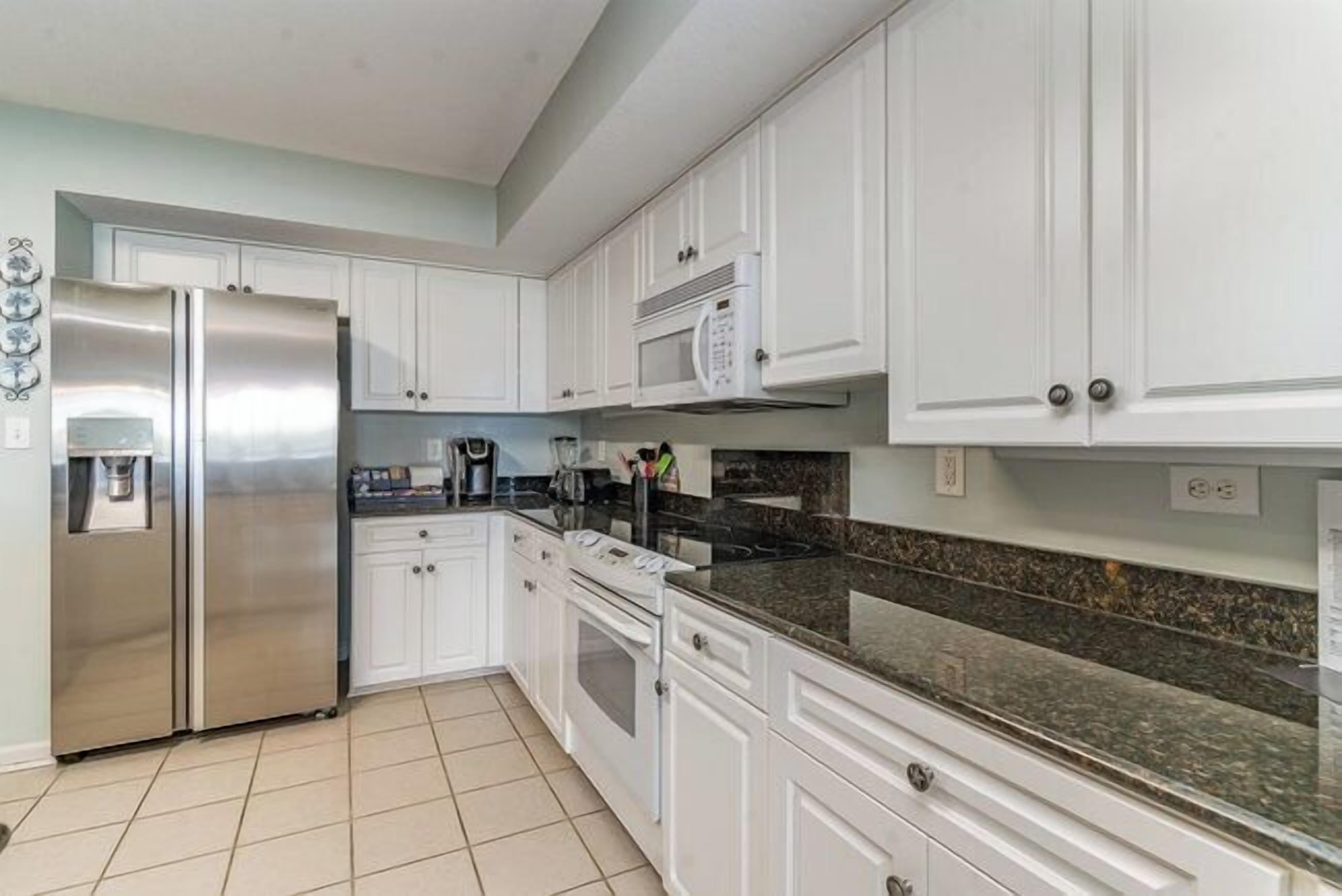 A kitchen with white cabinets, a stainless steel refrigerator, a microwave, and a granite countertop.