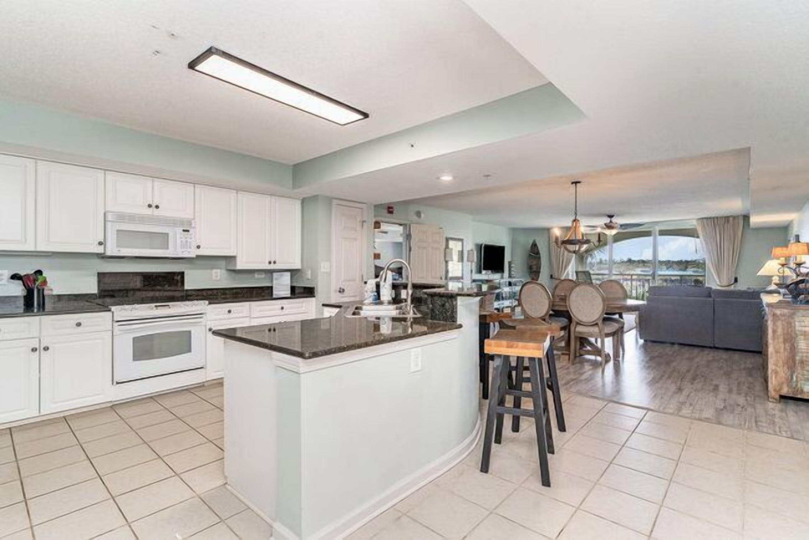A modern kitchen with white cabinets, a central island, and a dining area with a gray sofa and wooden chairs.