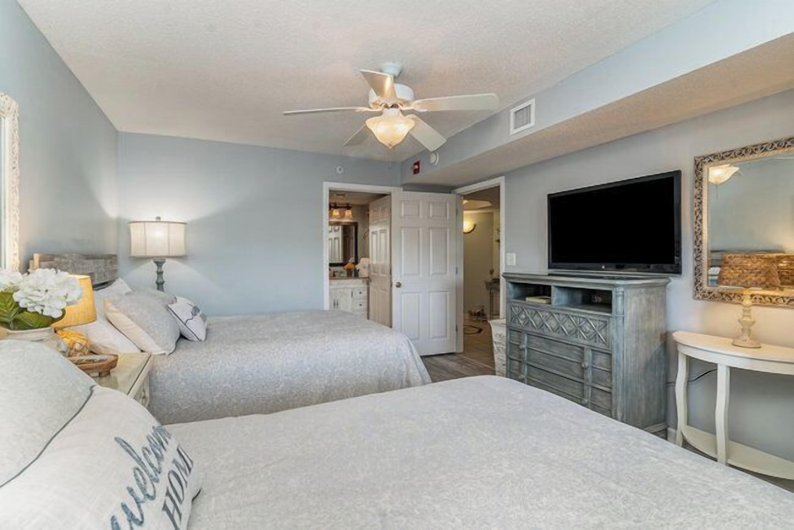 A hotel room with two beds, a ceiling fan, a television, and a fireplace.