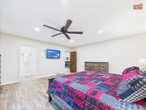 Un dormitorio con cama, ventilador de techo, televisor y cómoda de madera.