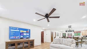 Una sala de estar amplia con televisor de pantalla plana, muebles de madera y ventilador de techo.