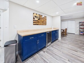 A modern kitchen with blue cabinets, a wooden countertop, and a heart-shaped artwork with 'MJ' on the wall.