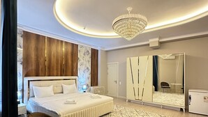 A modern hotel room with a large bed, a round table, two chairs, a chandelier, a large mirror, and a wardrobe. - Nur Makan Hotel Tashkent (Tashkent)