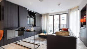 A modern living room with a dark wood cabinet, a glass-top coffee table, a black sofa, and a view of the outside through large windows. - A pop of colours (London)
