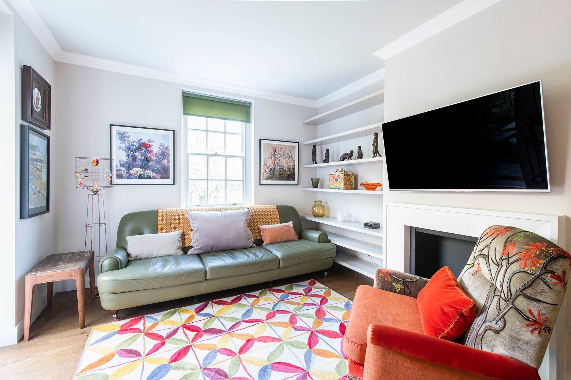 A living room with a green sofa, a colorful rug, a small wooden table, and a television on the wall.