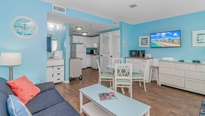 A living room with a sofa, a coffee table, and a TV. There is a kitchen area with cabinets and a microwave. - Myrtle Beach Resort RT1103 (Myrtle Beach)