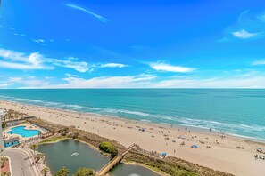 Uma praia com piscina, céu limpo e mar calmo.
