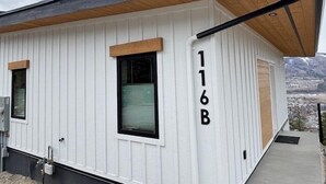 A modern building with a white exterior, a black roof, and a wooden overhang. The address "116B" is visible on the side. - Bungalow in the Bluffs (Penticton)