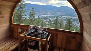 A wooden cabin with a large arched window overlooking a mountainous landscape and a body of water. - Bungalow in the Bluffs (Penticton)
