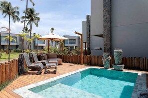 A pool area with lounge chairs, a wooden deck, and a stone wall. - Casa Kumari - By Living Milagres (Passo de Camaragibe)