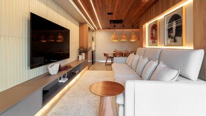 Een moderne woonkamer met een grote flatscreen televisie, een bank, een salontafel en hanglampen.