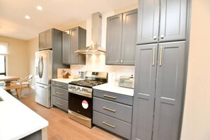 A modern kitchen with grey cabinets, stainless steel appliances, and a wooden dining table.