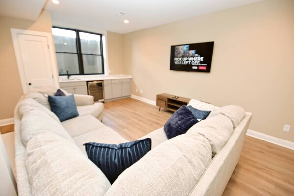 A living room with a beige sofa, a small wooden side table, and a TV mounted on the wall.