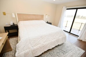Une chambre à coucher avec un grand lit, une table de chevet, un bureau et une vue sur un balcon, accessible par une porte coulissante.