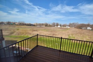 A balcony with a view of a grassy field and distant houses.