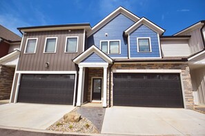 A two-story residential building with a garage entrance, a stone facade, and a clear blue sky.