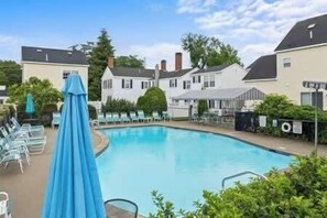 Une piscine entourée de maisons, avec des chaises longues et des parasols.