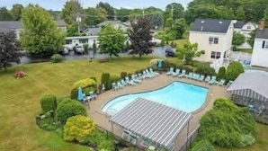 A swimming pool with a covered deck, surrounded by a grassy area and trees.