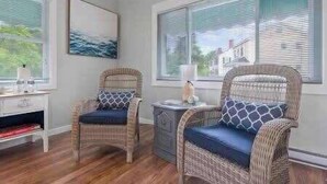 A room with two wicker chairs with blue cushions, a small table with a lamp, and a painting on the wall.