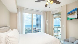 Une chambre d’hôtel avec un grand lit, un ventilateur de plafond, une vue sur l’océan et un immeuble imposant, ainsi qu’un balcon décoré d’une figurine d’hippocampe.