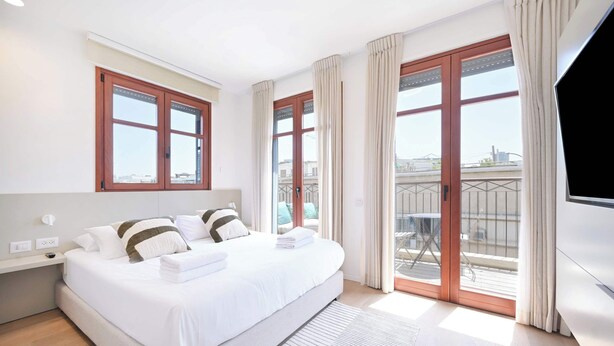 Una habitación de hotel moderna con una cama grande, un televisor de pantalla plana y un balcón con vistas a la ciudad.
