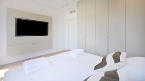 Una habitación de hotel moderna con una cama grande, un televisor de pantalla plana montado en la pared y un armario con puertas correderas.