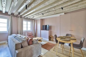 Ein modernes Wohnzimmer mit einer Couch, Sesseln, einem Fernseher und einem Esstisch.