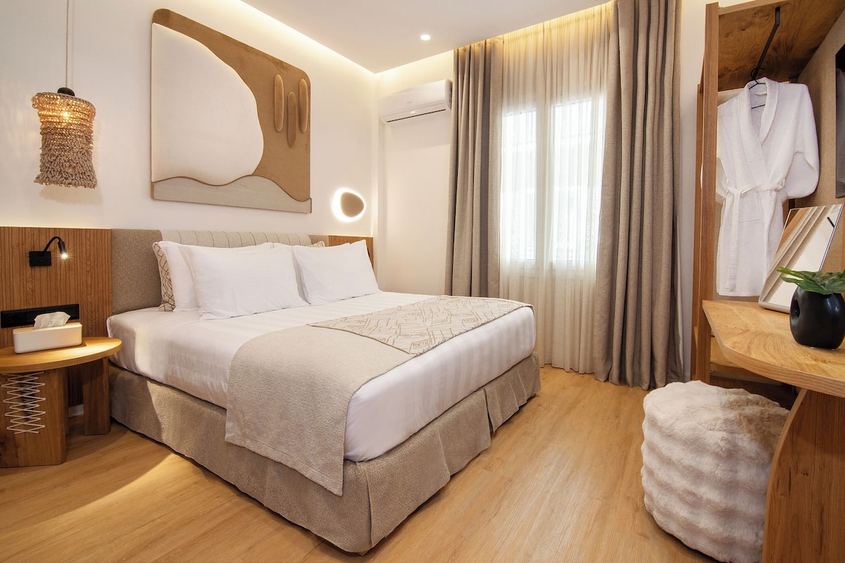 Une chambre à coucher moderne avec un grand lit, une table de chevet avec une lampe, un miroir et un porte-manteau mural.
