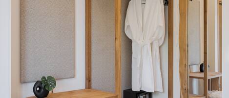 A bedroom with a wooden wardrobe, a bedside table, a fluffy white ottoman, and a large mirror.