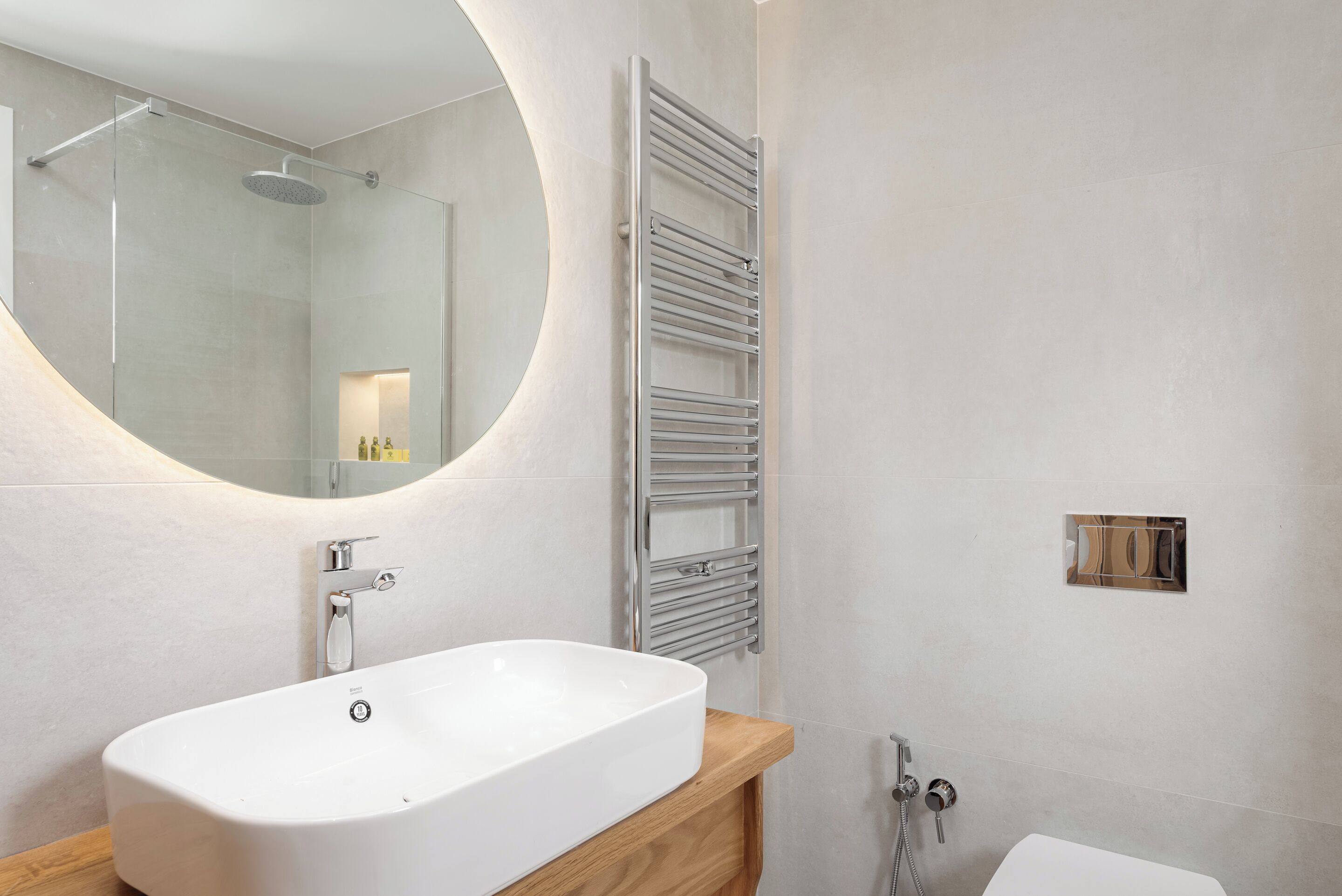 A modern bathroom with a freestanding bathtub, a round mirror, a towel rack, and a toilet.