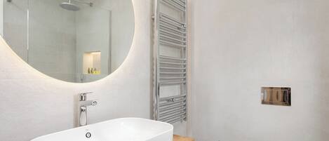 A modern bathroom with a freestanding bathtub, a round mirror, a towel rack, and a toilet.