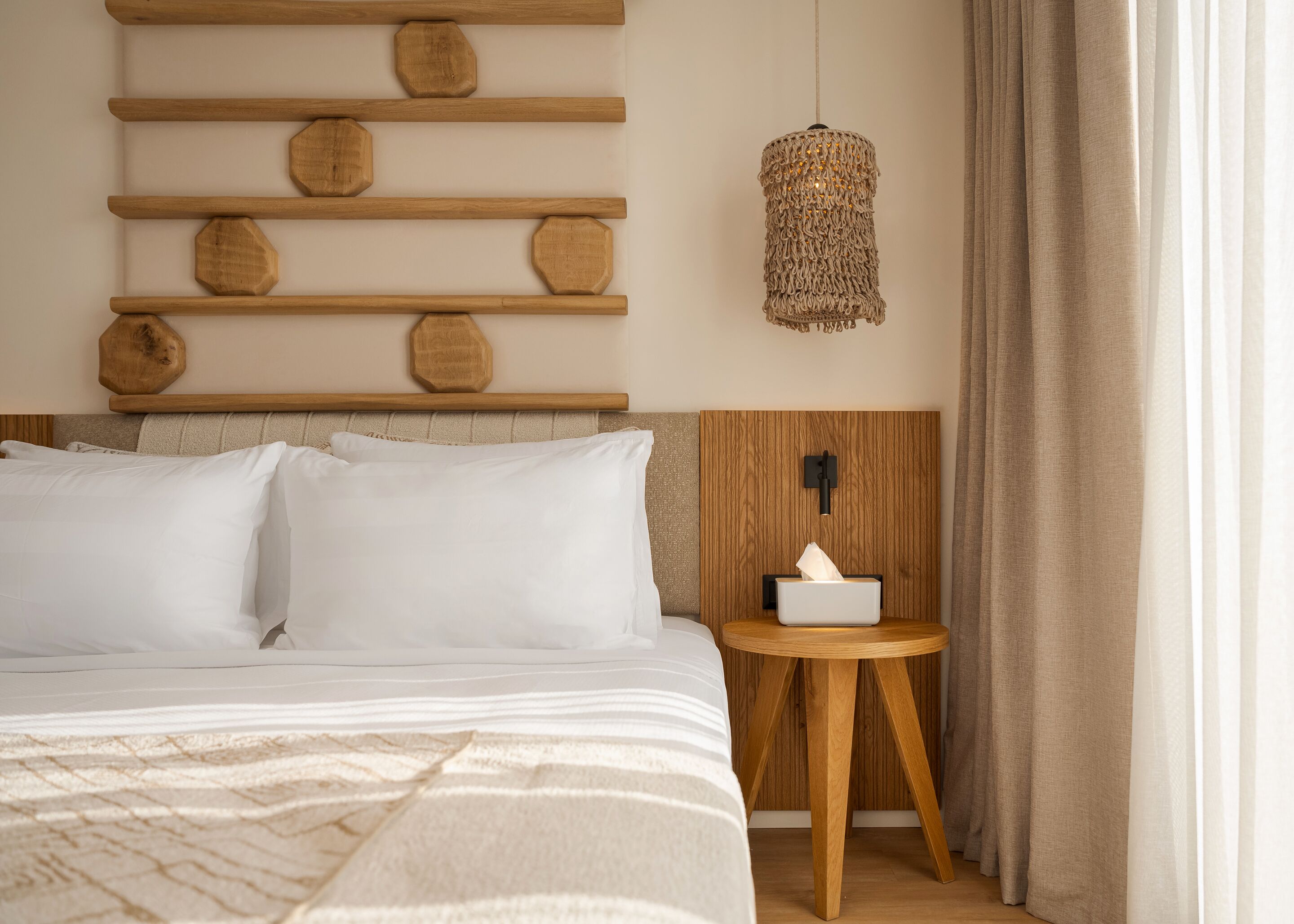 Una camera d'albergo ordinata con un letto, un comodino con una scatola di fazzoletti, una lampada a parete e una testiera in legno con decorazioni.