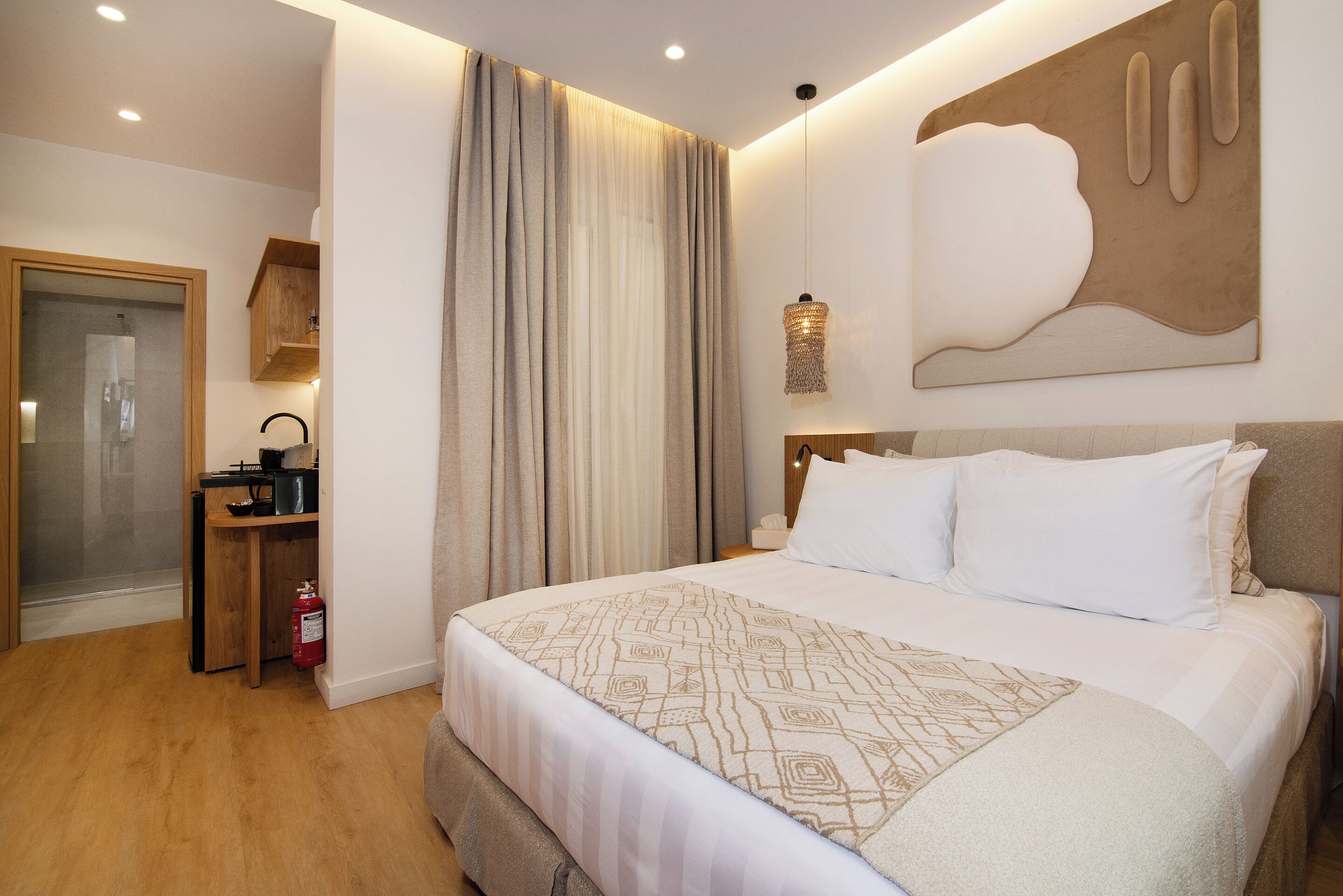 A modern hotel room with a large bed, a wooden desk, a shower area, and a wall-mounted artwork.