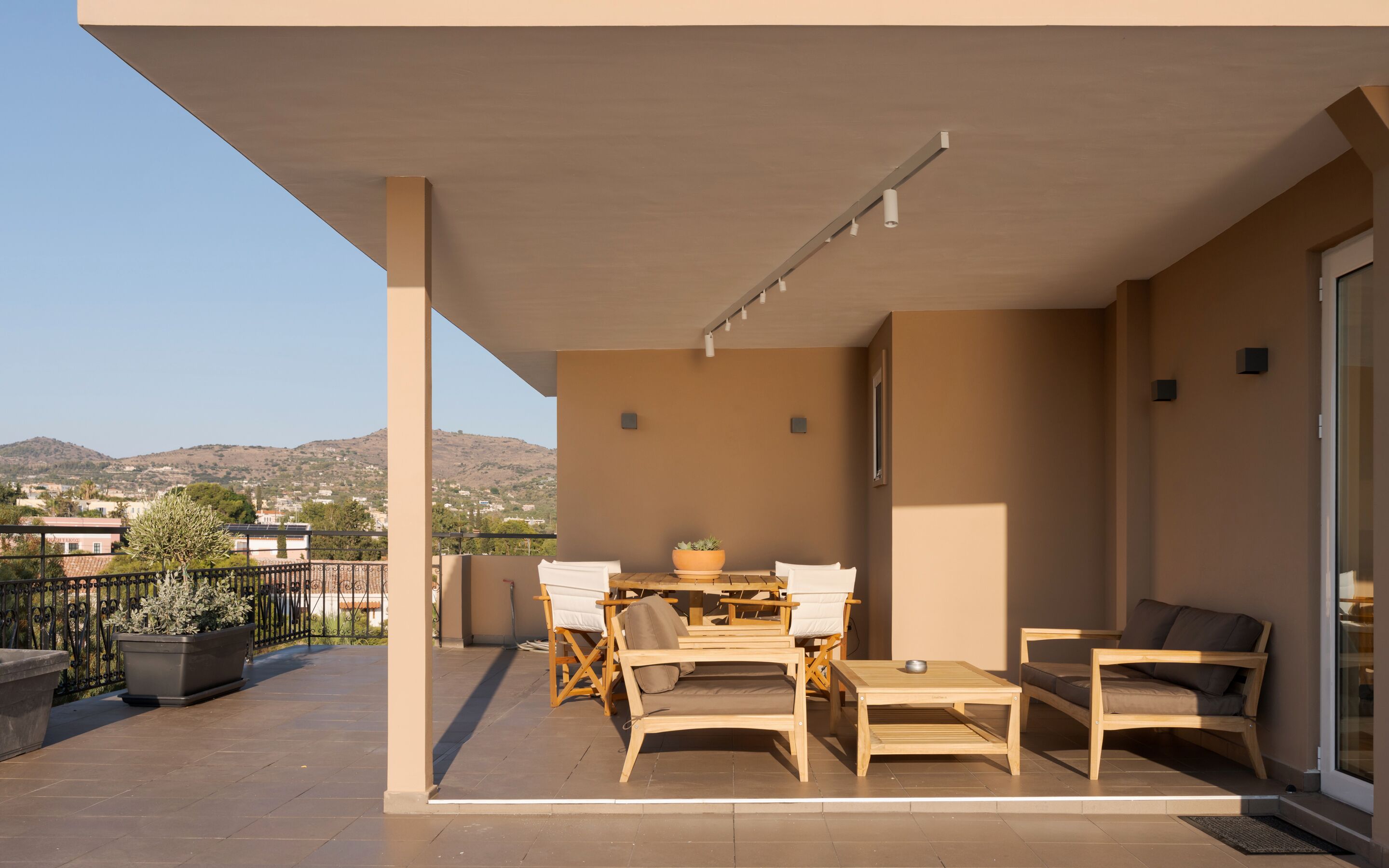 A covered outdoor seating area with a table and chairs, a potted plant, and a view of the surrounding landscape.