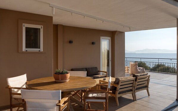 A balcony with a wooden table and chairs, a potted plant, and a view of the sea. - Aegina Dream Suites (Aegina)