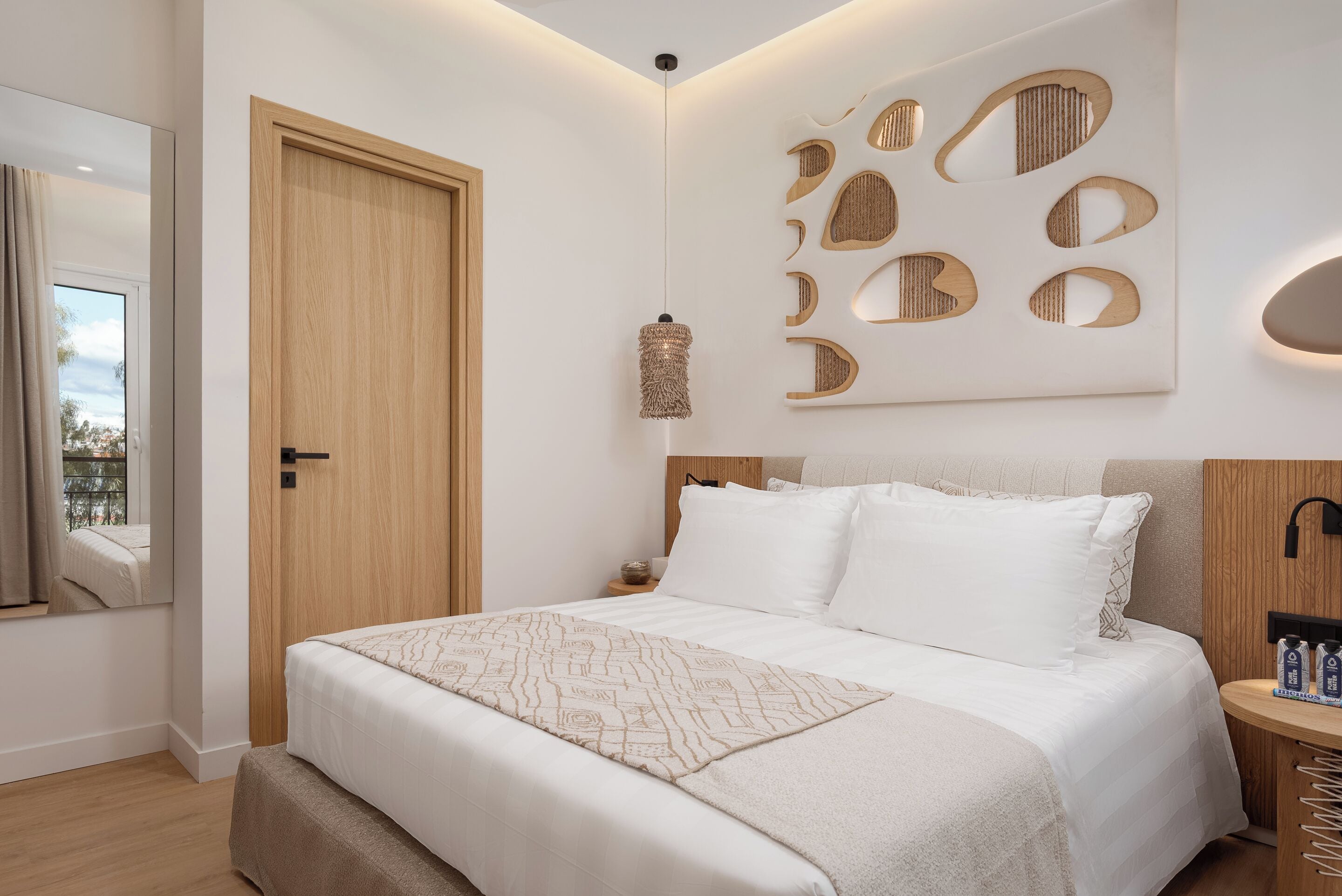 A bedroom with a bed, a wooden door, a wall-mounted light fixture, and a decorative wall panel.
