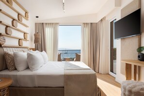 A modern hotel room with a large bed, a TV mounted on the wall, and a balcony with a view of the sea.