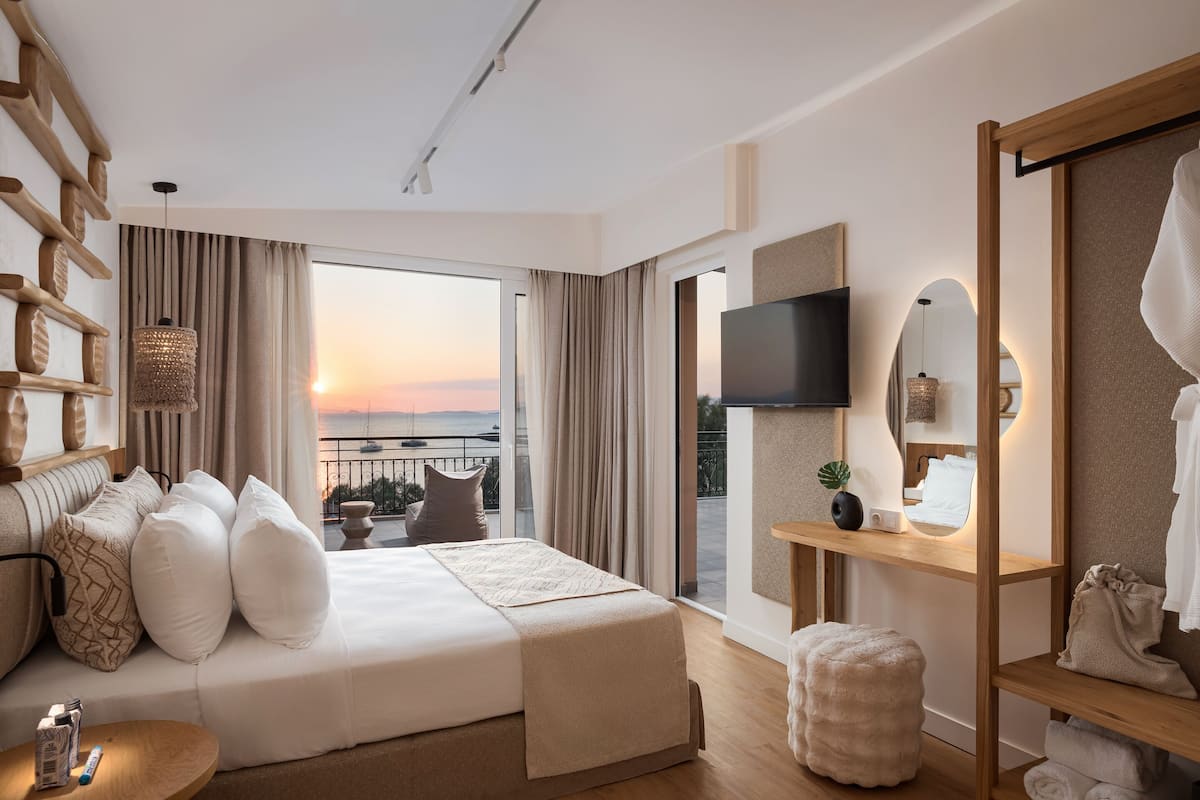 Une chambre d’hôtel moderne dotée d’un grand lit, d’une télévision, d’un balcon avec vue et d’une étagère en bois où sont rangées les serviettes.