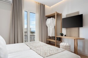 A modern hotel room with a large bed, a wooden shelf with a robe and a flat-screen TV, and a balcony with a view.