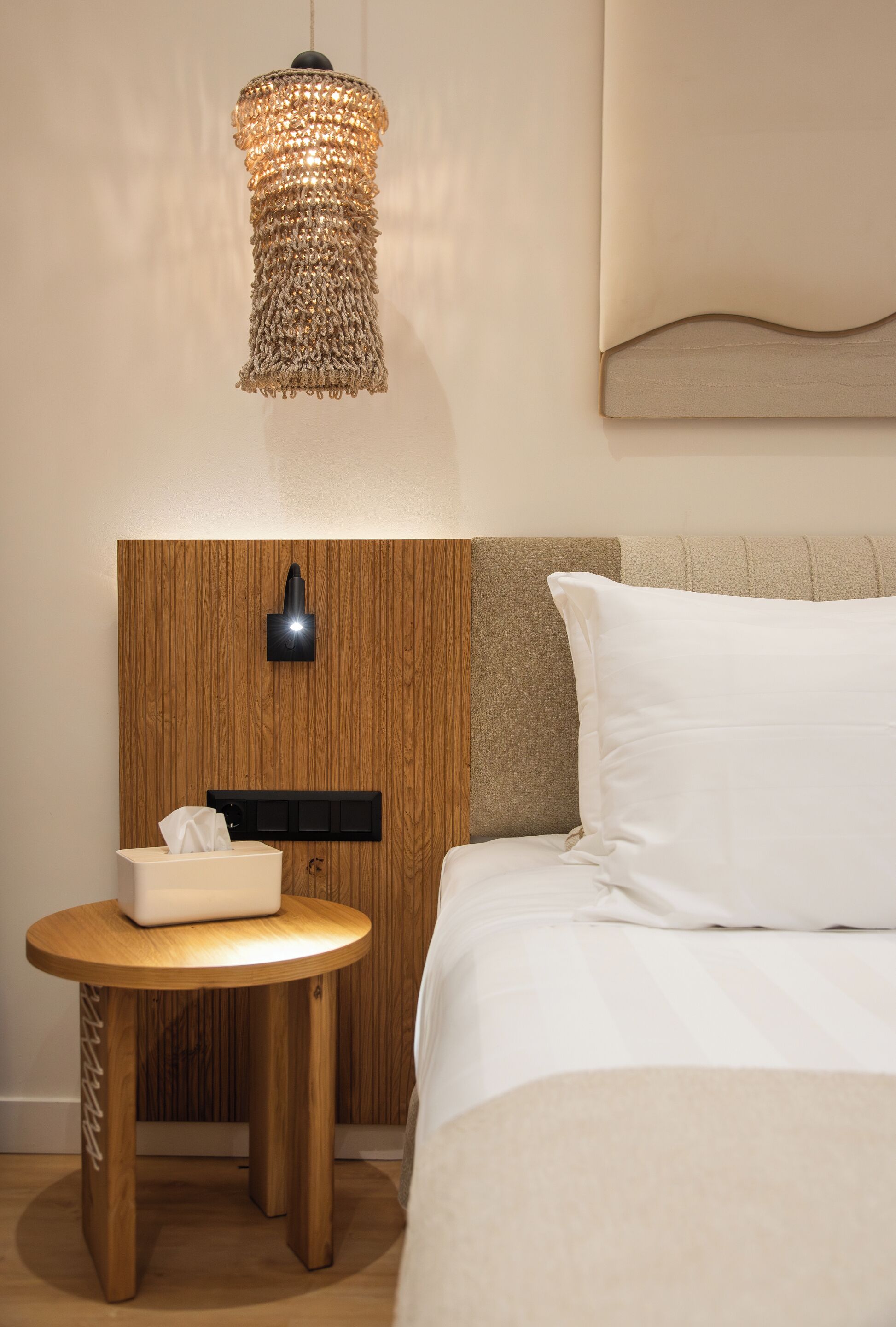 A neatly arranged hotel room with a wooden headboard, a bedside table with a tissue box, and a hanging light fixture.