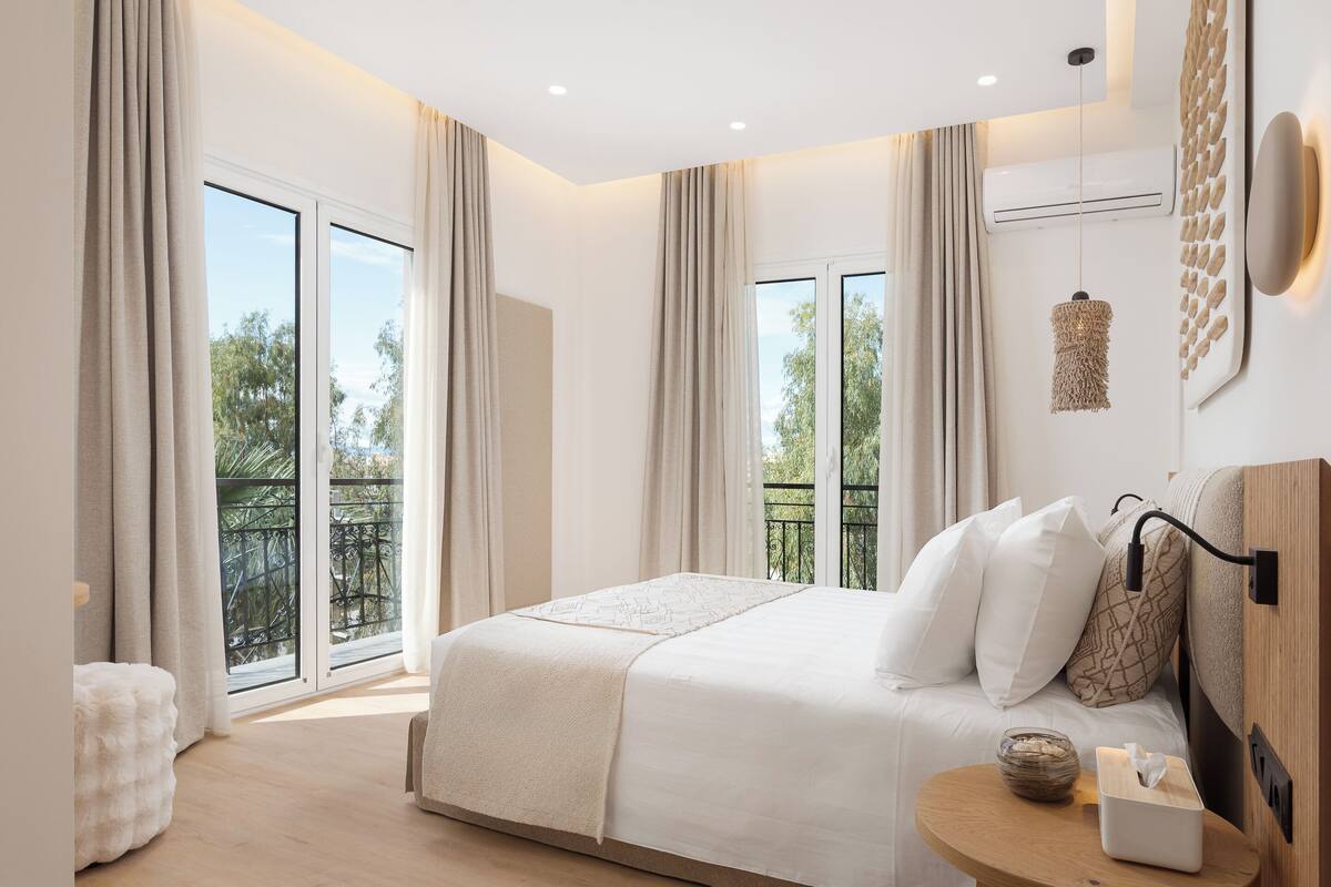 Une chambre avec un grand lit, une table de chevet sur laquelle se trouve une boîte de mouchoirs, et une vue sur un balcon.