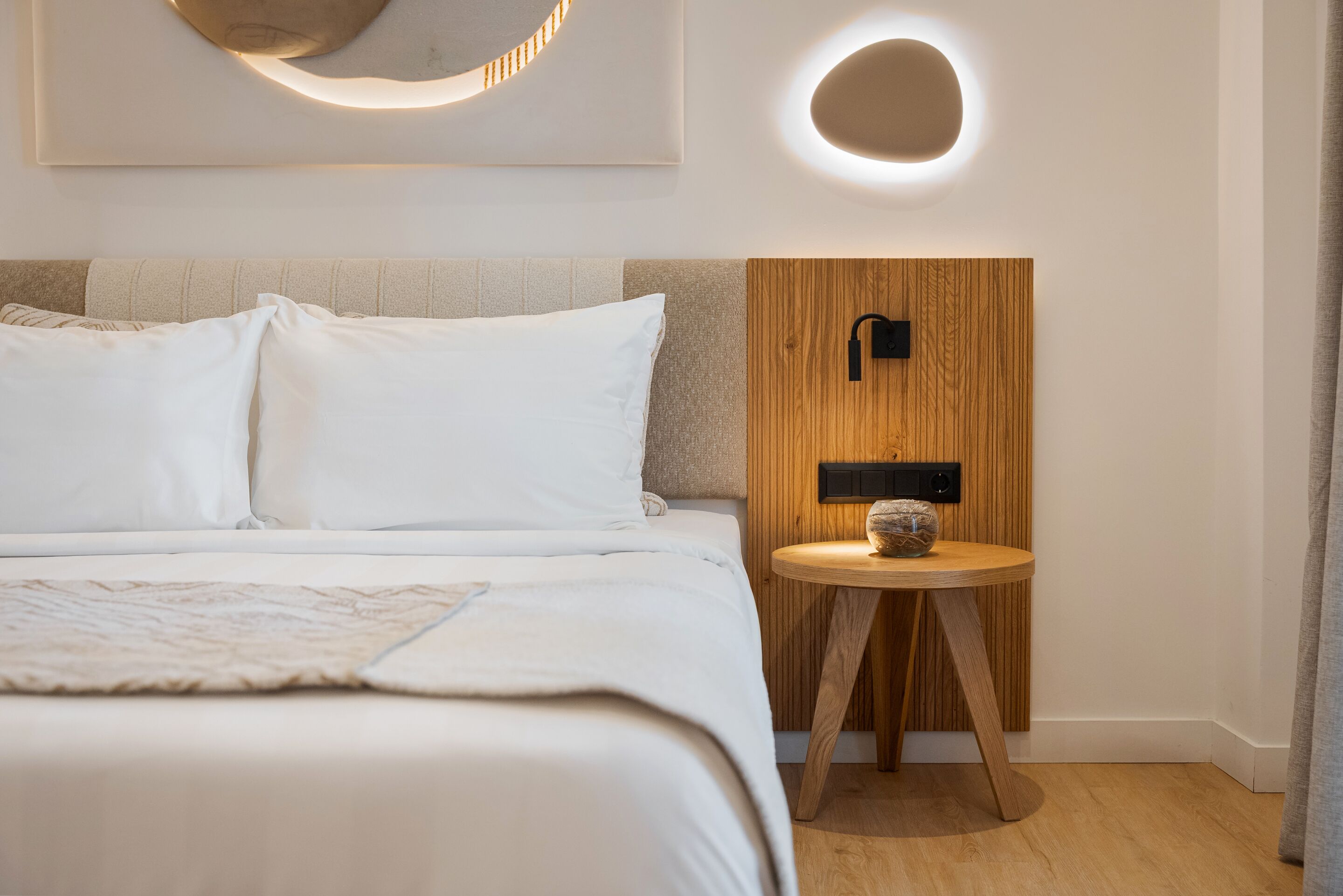 Ein modernes Schlafzimmer mit einem Bett, einem runden Tisch mit einer Vase und einer Wandleuchte.