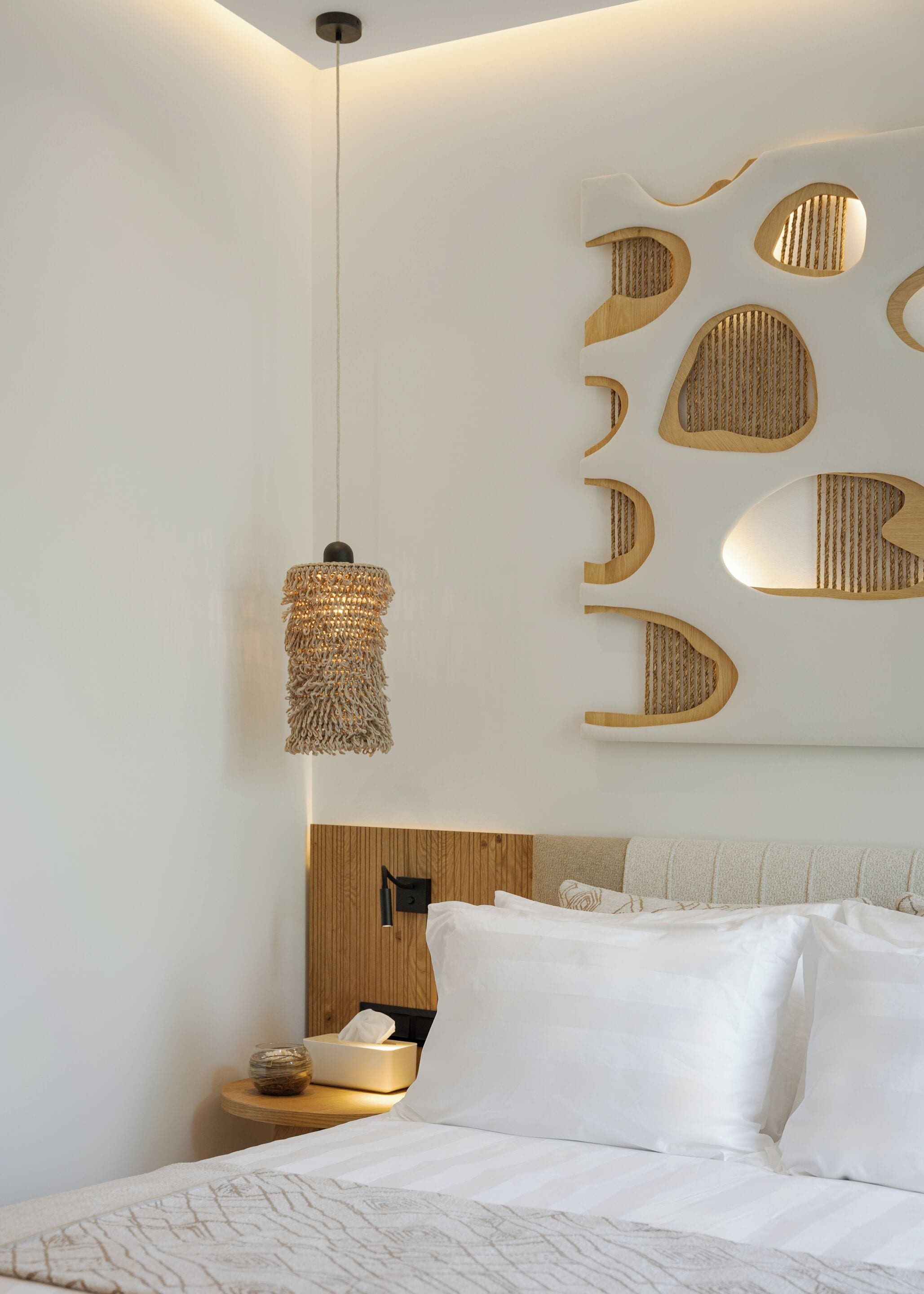 A modern bedroom with a wooden headboard, a hanging light fixture, and a wall-mounted shelf with decorative elements.